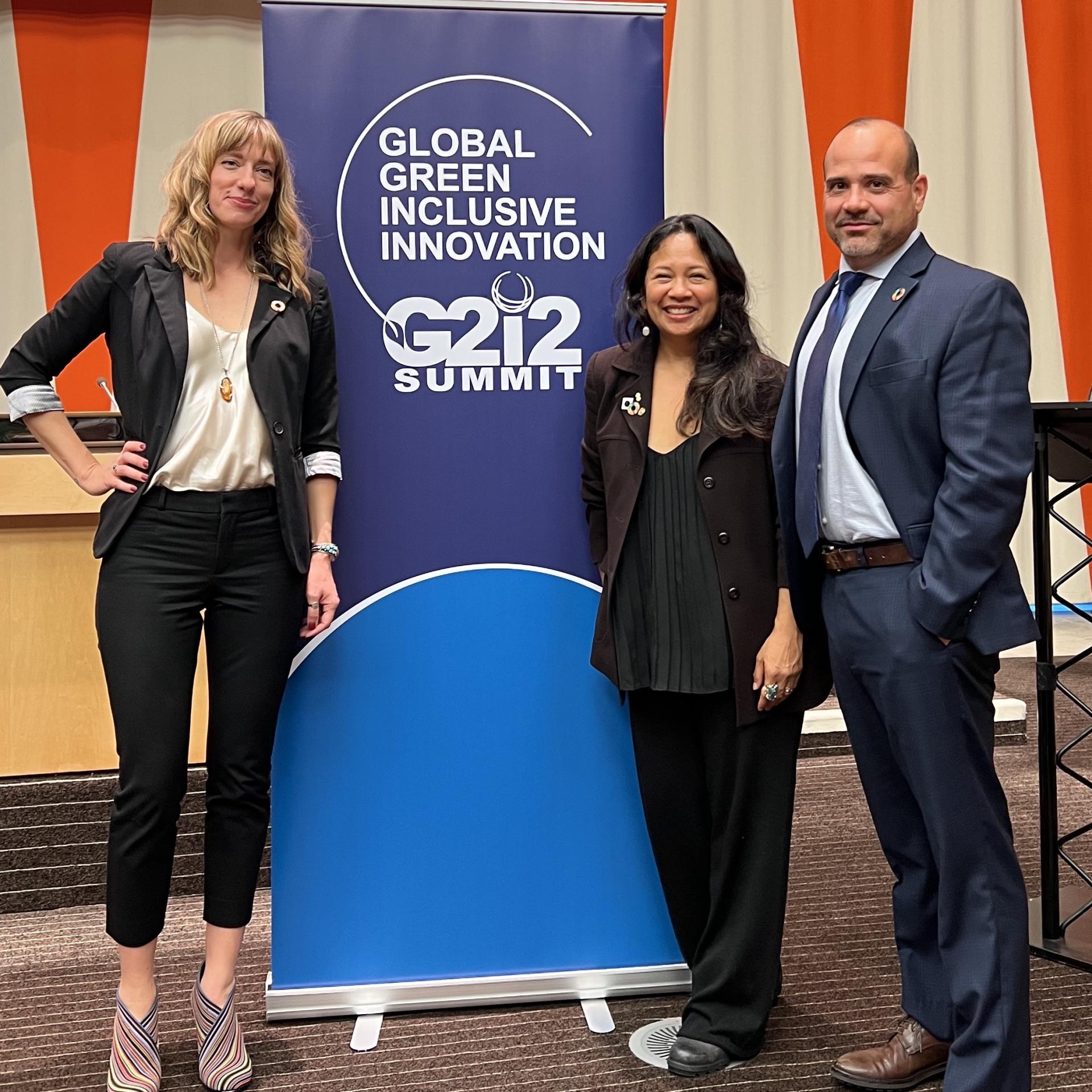 Lindsay Kent, Tess Mateo, and Anthony Bey stand in front of a G2i2 summit banner